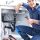 Plumber fixing kitchen sink pipes with tools in blue outfit and cap under sink cabinet